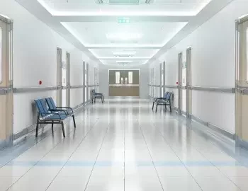 The corridor of a hospital with white tiled flooring.
