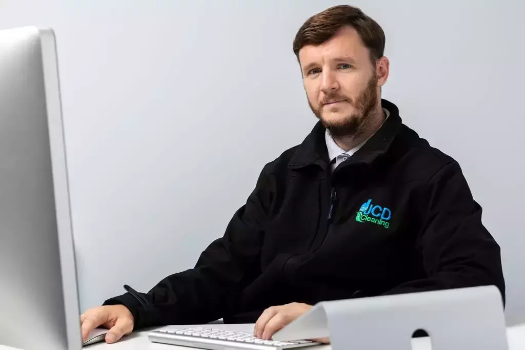 Chris Guilfoyle in the JCD Cleaning uniform, sitting at his desk.