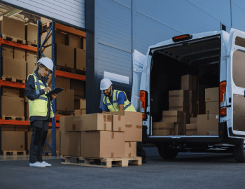 Warehouse personnel loading boxes off a van outside the back of a warehouse.