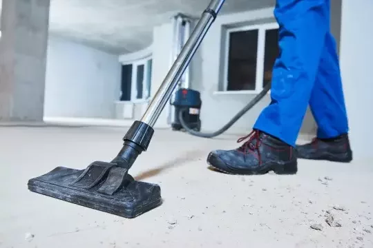 A post-construction cleaner uses a vacuum to clean the floor of a new build.