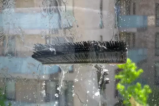 An extended water-fed pole with a brush cleans a window that is too high up to reach normally.