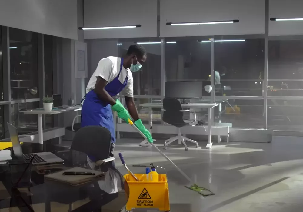 A man with a face mask mops an office floor.