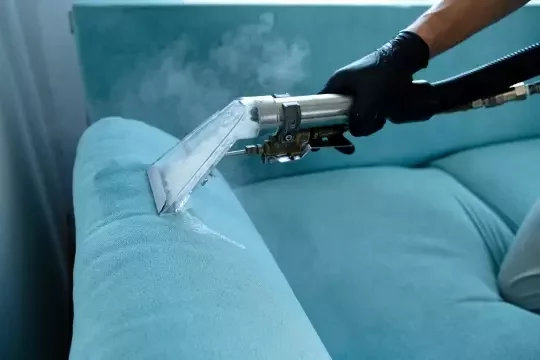 Deep cleaning steaming vacuum used to clean a blue sofa.
